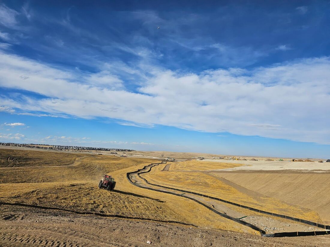 Tractor crimping straw on a graded slope beside a silt fence lined channel